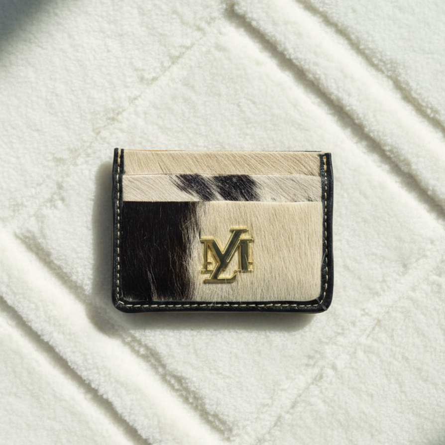 Cardholder with cowhide pattern and gold logo on a textured white surface